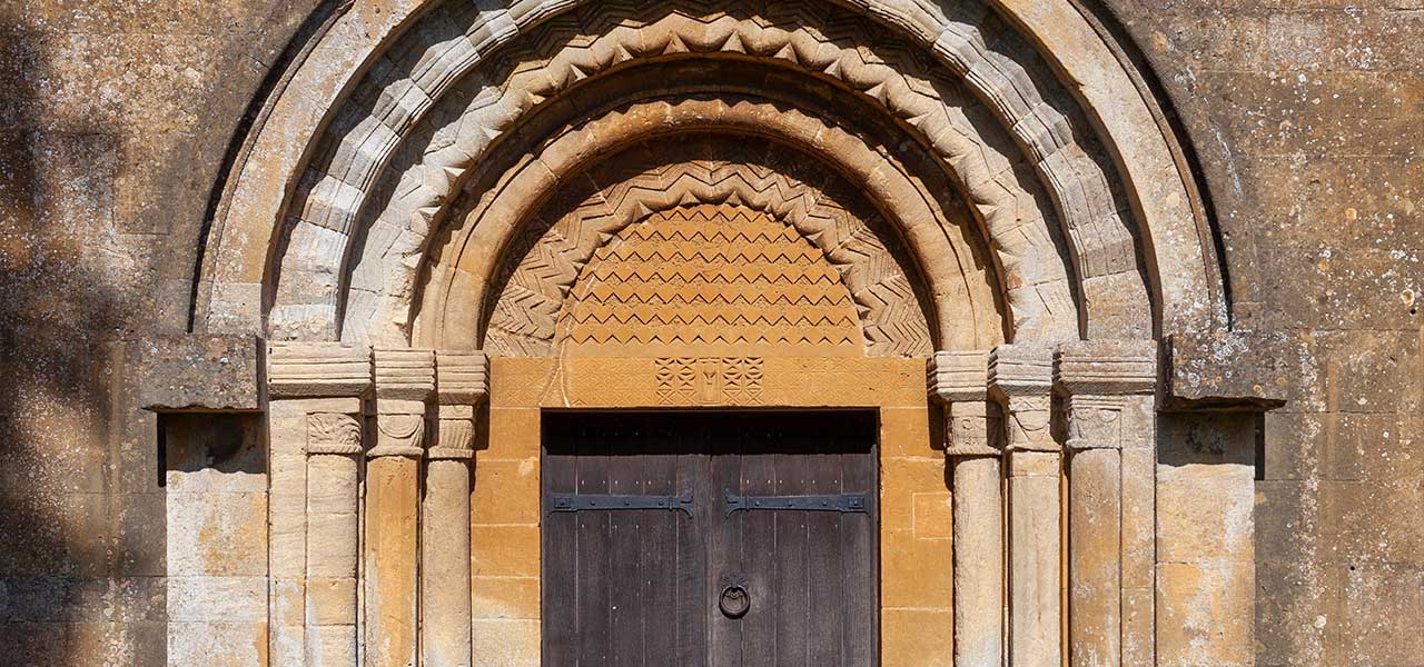 Carved Norman doorway with chevron-patterned arches and tympanum on a Cotswold stone church at St Michael and All Angels, Guiting Power